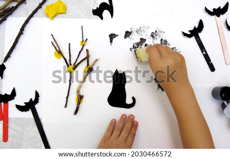 Child making card for the holiday  Halloween. Funny crafts from paper, natural tree twigs and painting with a sponge. The concept for Halloween. DIY. Children's art project, a craft for children.