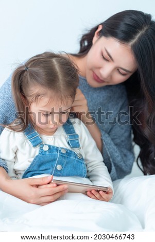 Stepmother take care lovely European foster adorable girl kid. Read stories, see cartoon online together by phone at bedroom with happy smiles. Love of Single mother or baby sister and stepchildren.