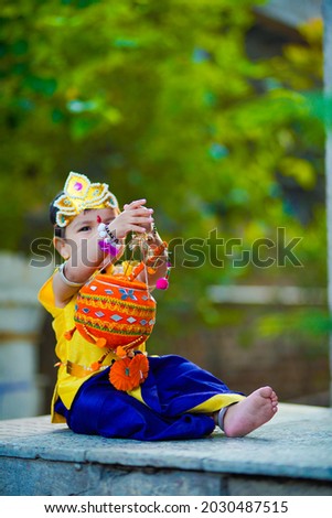 happy Janmashtami Greeting Card showing Little Indian boy posing as Shri Krishna or kanha or kanhaiya with Dahi Handi picture and colourful flowers.