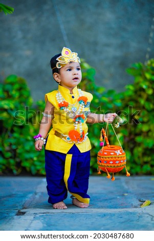 happy Janmashtami Greeting Card showing Little Indian boy posing as Shri Krishna or kanha or kanhaiya with Dahi Handi picture and colourful flowers.