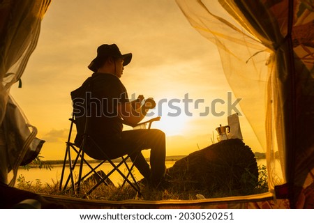 A traveler holds an iron jug with tea or coffee. Enjoy the sunset view of the sea landscape. Sit in a chair for travel, travel, camping and an adventurous lifestyle.