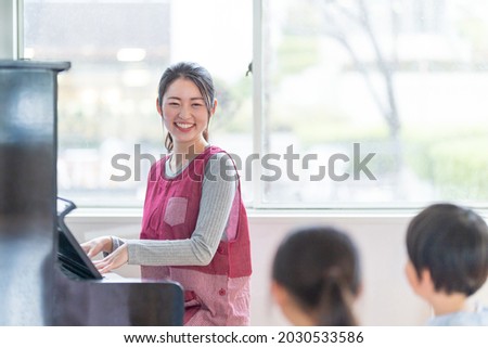 A nursery teacher playing the piano and a kindergarten singing Royalty-Free Stock Photo #2030533586