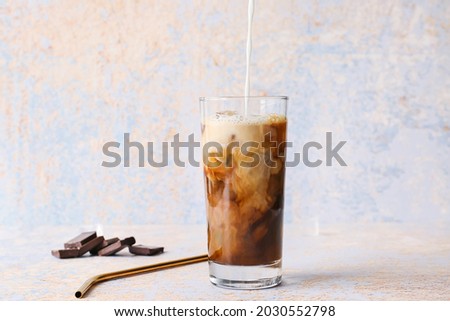 Pouring of milk into glass with hot coffee and chocolate on color background