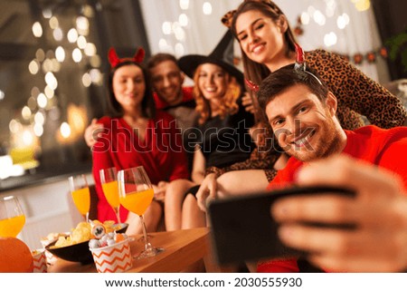 friendship, holiday and people concept - group of happy smiling friends in halloween costumes of vampire, devil, witch and cheetah taking selfie by smartphone at home party at night