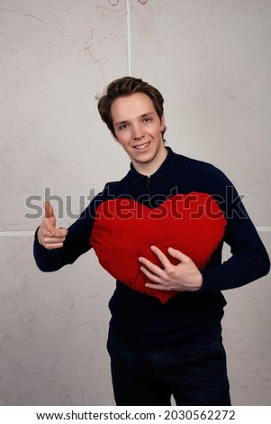 A young and enamored man with a heart in his hands. Valentine's day, gifts and cards. The guy on the background of a white loft wall.