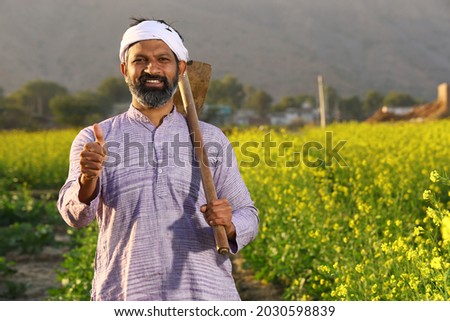 Beautiful dramatic portrait of Indian rural happy farmer standing in mustard field wearing kurta pajama in summer time. Pleased farmer is holding shovel in hand. Flourishing crops. Royalty-Free Stock Photo #2030598839