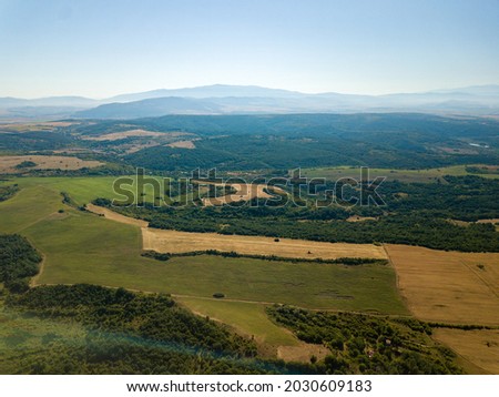 An aerial view of agricultural fields, with dense trees and mountains under a blue clear sky
