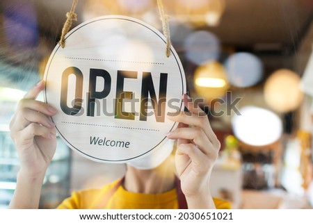 friendly asain staff woman wearing protection face mask turning open sign board on glass door in modern cafe coffee shop, hotel service, cafe restaurant, retail store, small business owner concept
