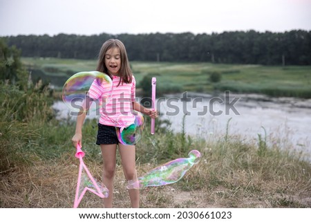 A little girl makes big multi-colored soap bubbles in the nature outside the city, active leisure in summer.