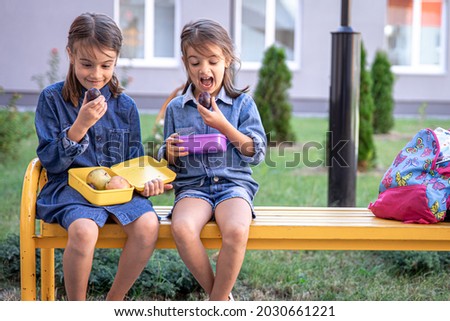 Back to school. Cute little school girls sitting on bench in school yard and eating lunch outdoor. Right school meal for lunch. Royalty-Free Stock Photo #2030661221