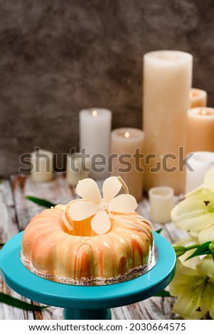 Beautiful cake with beige glaze, decorated with flowers from white chocolate on cake stand on a wooden background. Place for text