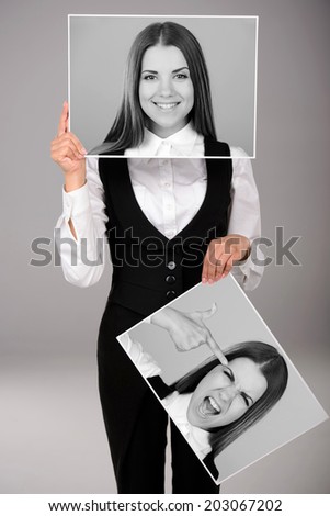 A young business woman holds two portraits of different emotions to choose from today. Gray background
