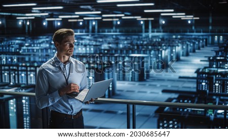 Data Center Specialist Engineer Using Laptop Computer. Server Farm Cloud Computing Facility with Male Maintenance Administrator Working. Data Protection Network for Cyber Security. Royalty-Free Stock Photo #2030685647