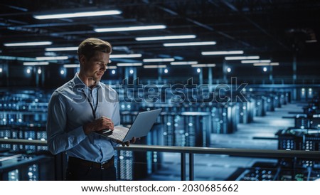 Data Center Specialist Engineer Using Laptop Computer. Server Farm Cloud Computing Facility with Male Maintenance Administrator Working. Data Protection Network for Cyber Security. Royalty-Free Stock Photo #2030685662
