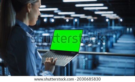 Female It Specialist Using Chroma Key Laptop in Data Center. Big Server Farm Cloud Computing Facility with Maintenance Engineer Working with Green Screen Computer.