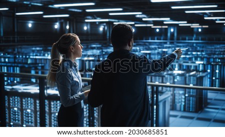 Data Center Male It Specialist and Female e-Business Fintech Startup Manager Talk, Use Laptop. Cloud Computing Server Farm with Two Information Technology Professionals working. Royalty-Free Stock Photo #2030685851