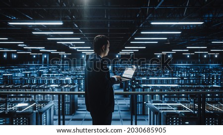 Data Center Male Administrator Using Laptop Computer. Maintenance Specialis working in Cloud Computing Facility on Cyber Security and Network Protection. Server Farm Analytics. Medium Wide
