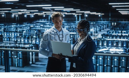 Data Center Female System Administrator and Male IT Specialist talk, Use Laptop. Information Technology Engineers work on Cyber Security Protection in Cloud Computing Server Farm. Royalty-Free Stock Photo #2030694494