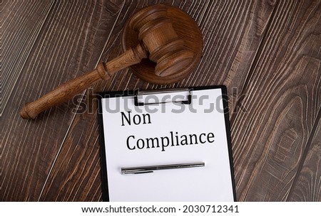NON COMPLIANCE text on the paper with gavel on wooden background