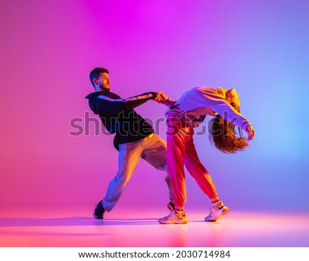 Smooth movements. Two young people, guy and girl, dancing contemporary dance over pink background in neon light. Modern dance aesthetics concept Royalty-Free Stock Photo #2030714984