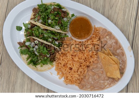Overhead view of hearty plate of three loaded carne asada tacos with cilantro, served with rice and refried beans. Royalty-Free Stock Photo #2030716472