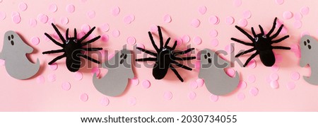 Halloween card with black spiders, grey ghost and confetti on pink background, flat lay, copy space, top view, banner