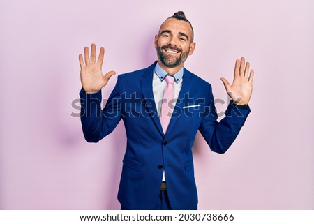 Young hispanic man wearing business suit and tie showing and pointing up with fingers number ten while smiling confident and happy. 
