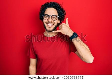 Handsome hispanic man wearing casual t shirt and glasses smiling doing phone gesture with hand and fingers like talking on the telephone. communicating concepts. 