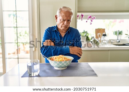 Senior man with grey hair eating pasta spaghetti at home skeptic and nervous, disapproving expression on face with crossed arms. negative person.  Royalty-Free Stock Photo #2030751971