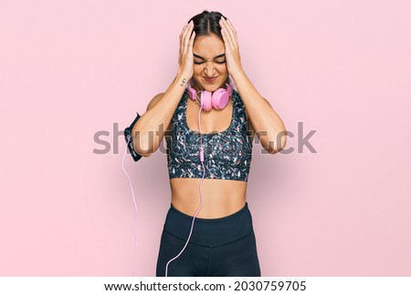Beautiful brunette woman wearing gym clothes and using headphones suffering from headache desperate and stressed because pain and migraine. hands on head. 