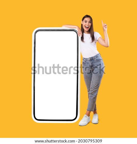 Wow. Happy Woman Leaning On Big Smartphone With Blank White Screen And Pointing Finger Up, Cheerful Lady Recommending New App Or Website, Standing On Yellow Background, Mock Up Image, Full Body Length Royalty-Free Stock Photo #2030795309
