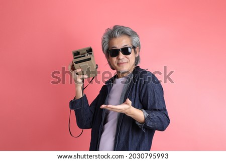 The Asian man standing on the pink background.