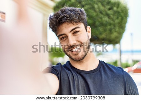 Young hispanic man smiling happy making selfie by the camera at the city.