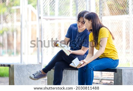 On a campus, a couple of students are studying together, and a teenager sits on a seat beside a sports court with a book.