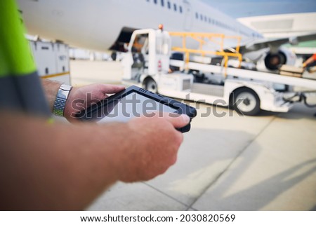 Member of ground staff preparing passenger airplane before flight. Worker using tablet against plane at airport. Royalty-Free Stock Photo #2030820569