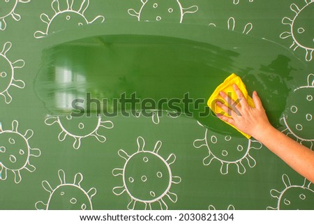A part of a green blackboard with a picture of coronavirus molecules washed with a wet yellow rag in a human hand and a space for copying. Concept-Back to School and stop covid-19
