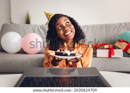 Happy Birthday. African American Female Making Wish Holding B-Day Cake In Front Of Laptop Computer Having Online Party Via Video Call At Home. Remote Holiday Celebration