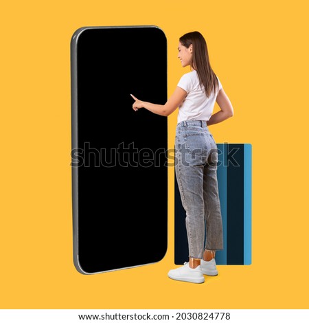 Full Body Length Of Happy Woman Touching Display Of Big Smartphone With Blank Black Screen And Credit Card, Cheerful Lady Using App Or Website, Paying Online, Standing On Yellow Background, Mock Up Royalty-Free Stock Photo #2030824778