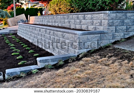 retaining wall concrete blocks gray 2 tier wall staggered side view new construction existing garden landscape    Royalty-Free Stock Photo #2030839187