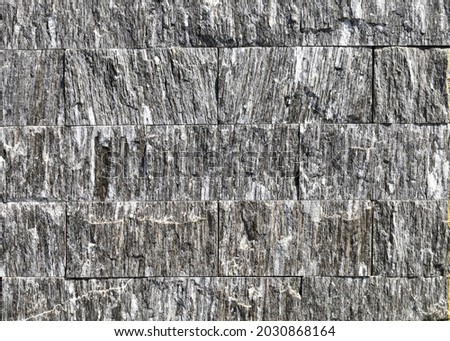 Tiles for exterior wall made of rough dark gray rock streaked with white. Background and texture.