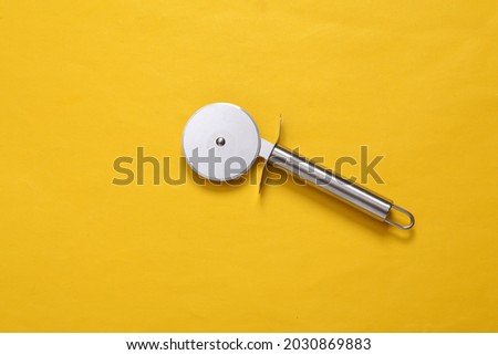 Steel round knife for cutting pizza on yellow background
