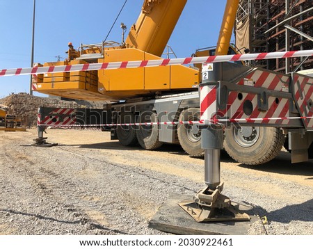 Outriggers of heavy all-terrain mobile crane at construction site. Crane work execution area fenced with a signal tape. Exclusion dropped zone Royalty-Free Stock Photo #2030922461