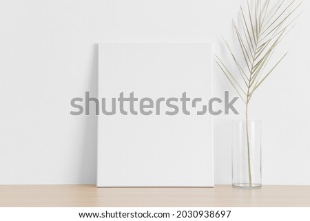 White canvas mockup with a palm leaf on the wooden table.
