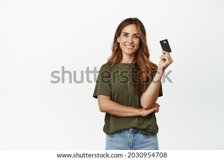 Image of smiling woman easy paying contactless, showing credit card and looking carefree, buying with discount, standing against white background