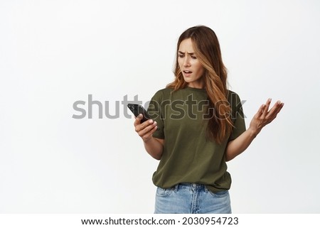 Annoyed and frustrated woman looking at mobile phone screen, complaining at smartphone cellular, speaking irritated, standing against white background Royalty-Free Stock Photo #2030954723