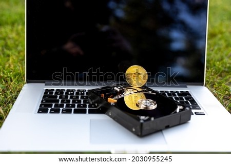 View on a laptop and a hard disk drive with a bitcoin representing cryptocurrencies on the grass on a sunny day.