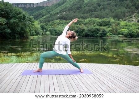 woman engaged in meditate in yoga posedd outdoor in the wood flooring against view of lake and rock