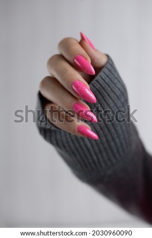 Female hand with long nails and a bottle bright neon pink red color nail polish