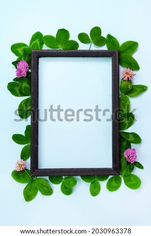 Black paper frame copy space. Flat lay, blue background. With clover petals. Vertical photo