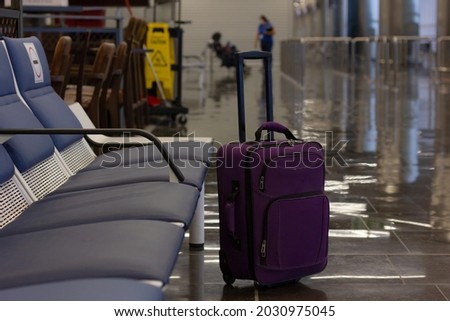 Unattended small carry on lugagge by empty bench seats at airport terminal. Purple suitcase left alone, security hazard concepts Royalty-Free Stock Photo #2030975045
